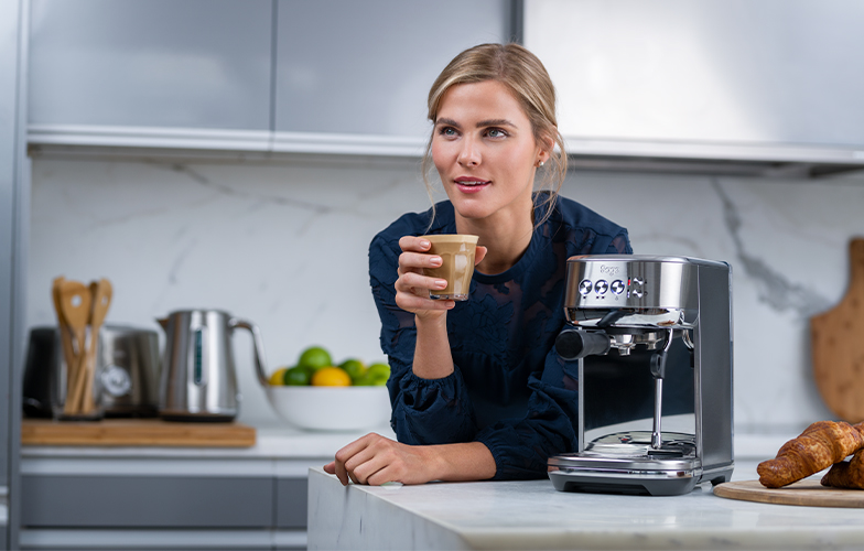 Woman with the Bambino™ Plus on kitchen bench holding latte