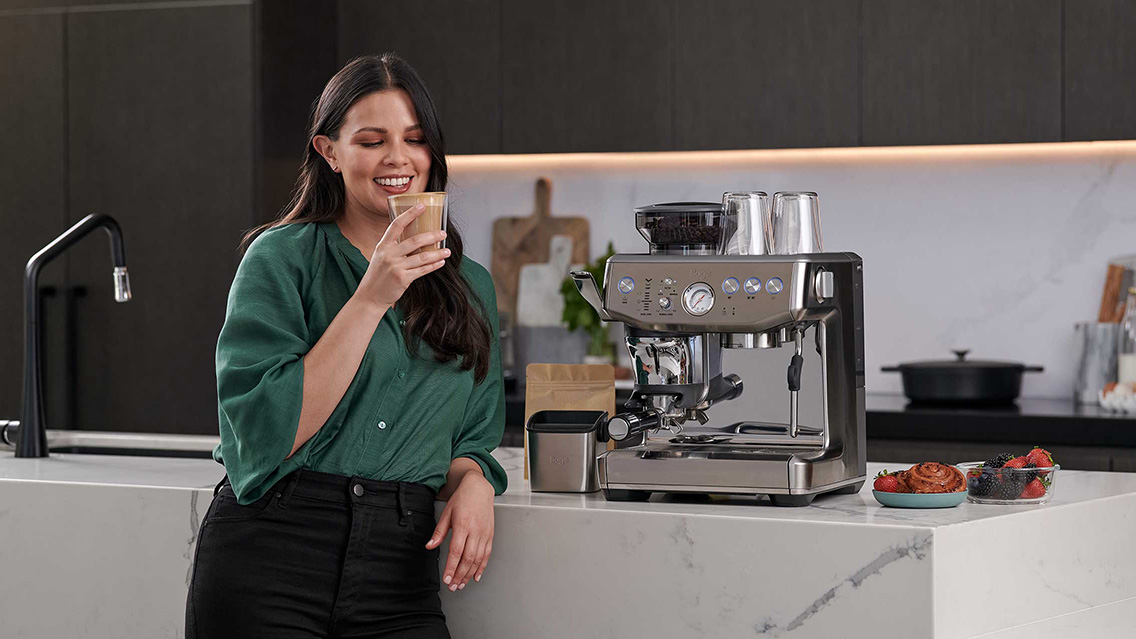 Woman holding a cup of coffee next to the machine.